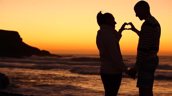 Couple making a silhouette heart shape with hands at seaside at sunset in Fue