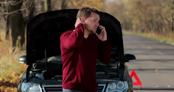 Young Unhappy Man Using Smartphone Calling Car Assistance Services Standing By Breakdown Automobile