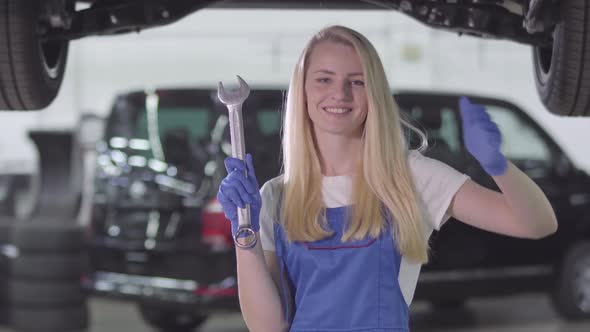 Smiling Female Auto Mechanic in Workrobe Holding Wrench and Showing Thumb Up. Blond Caucasian Woman