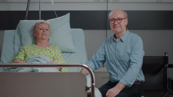 Portrait of Old Woman in Hospital Ward Bed and Husband Assisting Her