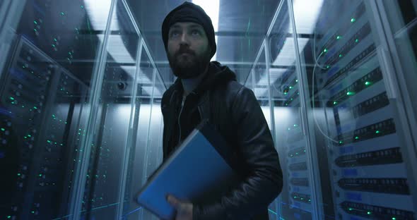 Hacker Sneaking Through Rows of Servers with Laptop