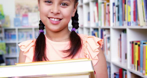 Portrait of schoolgirl holding stack of book in library at school