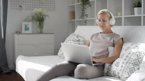 Woman in Headphones Sitting on Sofa and Typing on Laptop