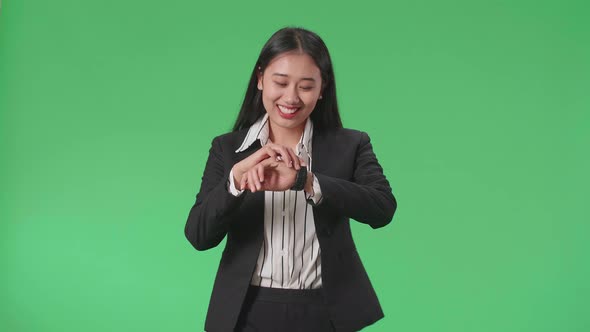 A Smiling Asian Business Woman Looking At A Watch While Walking On Green Screen Studio
