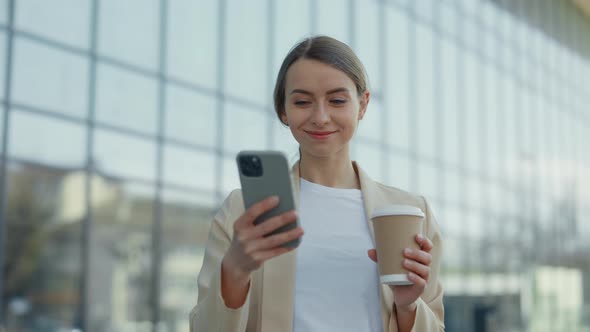 Woman with Coffee Standing Outdoors and Using Mobile