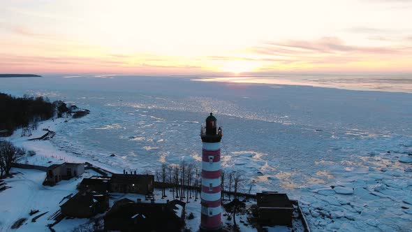 Red and White Lighthouse Stands on Island Against Frozen Sea