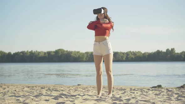 Smiling Caucasian Woman in VR-glasses Standing on River Beach and Hugging Someone Invisible. Wide