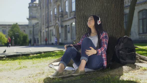 Asian Female in Headphones Enjoying Music, Sitting Under Tree, Favorite Band