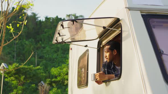 Asian young man feeling relax on camper van drinking coffee in the morning and smile on vacation.