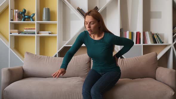 Woman Sitting on the Gray Couch in the Living Room and Holding Her Low Back