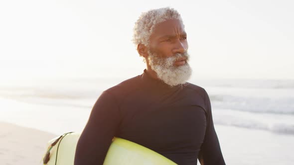 Happy senior african american man walking with surfboard on sunny beach