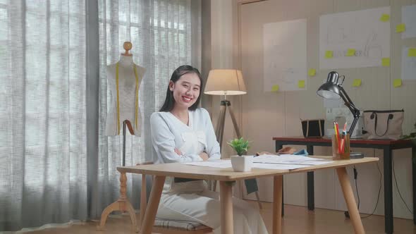 Asian Woman Designer Look At The Layout Bond, Cross Arms, And Smile To Camera While Working