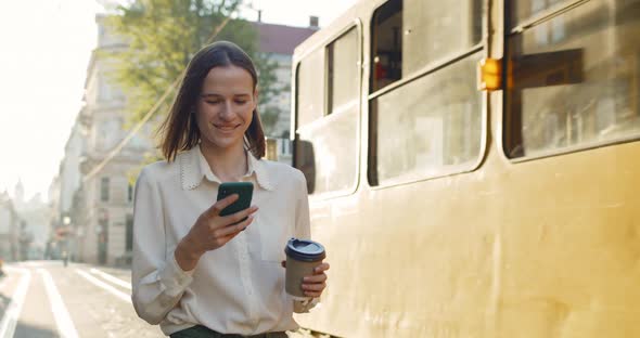 Young Girl Using Smartphone and Smiling While Tram Passing By Her. Atrractive Millennial Woman with