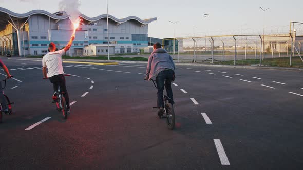 Young Friends are Riding Bmx Bicycles By Road Leading to a Trading Center and Doing Tricks Holding