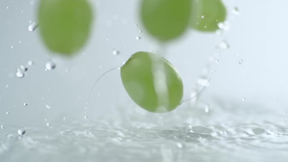 Green grapes falling and bouncing on water surface. Slow Motion.