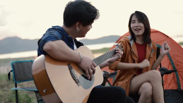 A happy young Asian couple backpacker playing the guitar and singing a song together.