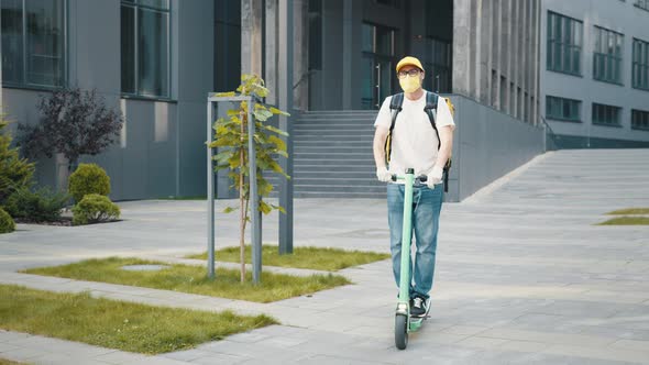 Delivery Man with Yellow Backpack and Protective Mask Riding Electric Scooter