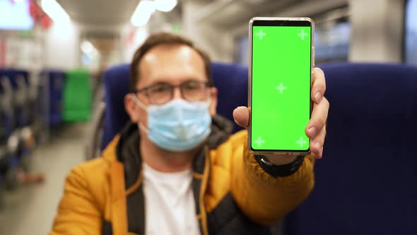 Millennial Man in Mask Rides on Train and Presents Phone with Chromakey to Camera