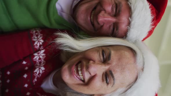 Flipped sideways portrait of happy senior caucasian couple celebrating christmas wearing santa hats