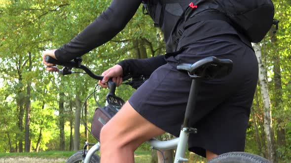 A Cyclist Stands with a Bike on a Path in a Forest and Looks Around - Closeup From Below