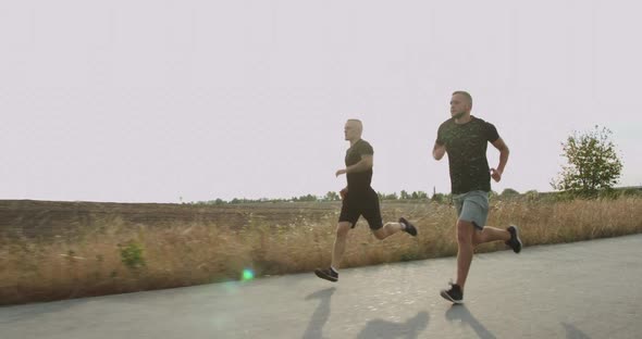 Two Sportsmen Jogging on Asphalt Walkway at Nature on Sunset