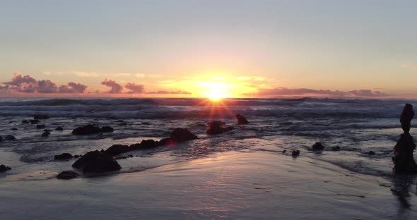 Stunning view of the sunset at low tide in Laguna Beach as the sun peaks out amongst rocks and refle