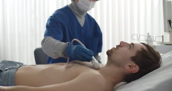 Doctor in Safety Mask and Gloves Performing Thyroid Ultrasound Test on Male Patient