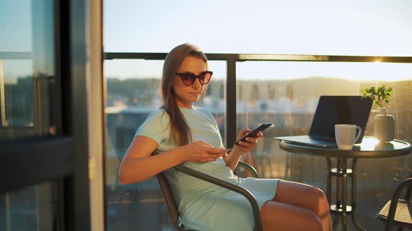 Woman Sitting on the Balcony Against the Backdrop of the Setting Sun and Makes an Online Purchase