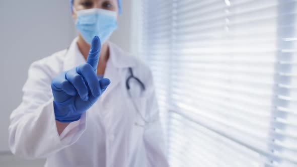 Caucasian female doctor wearing face mask and surgical gloves touching screen