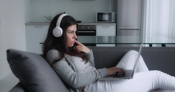 Full Side View of Darkhaired Aucasian Woman Sitting on the Sofa at Home Typing on Keyboard of