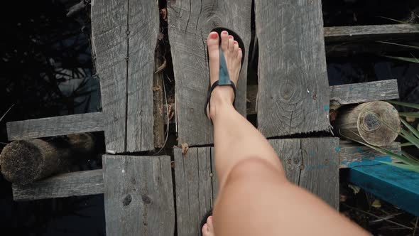 The Feet of a Woman are Walking Along a Narrow Wooden Bridge Over a River POV Video