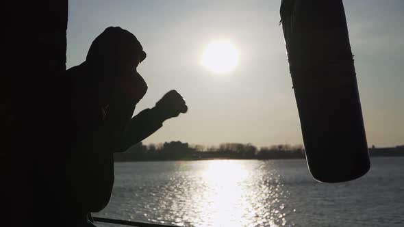 Silhouette. The boxer beats on a Boxing pear at the beautiful sunset and the river.