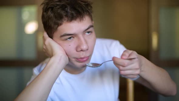 Teenager lazily puts rice porridge in his mouth and chews it