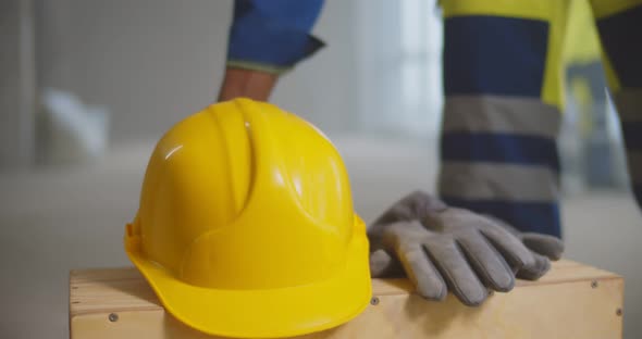 Close Up of Builder Putting Safety Hardhat and Gloves on Wooden Box