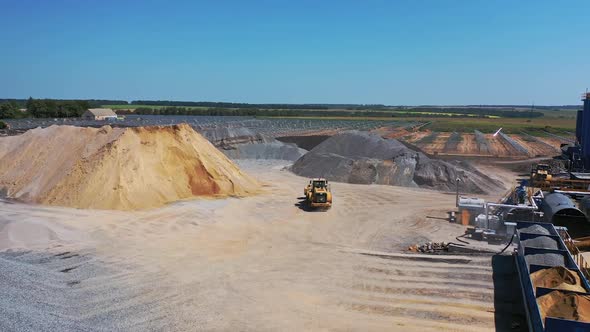 Excavator on the quarry. Big territory of asphalt factory. Piles with sand and rubbles outdoors.