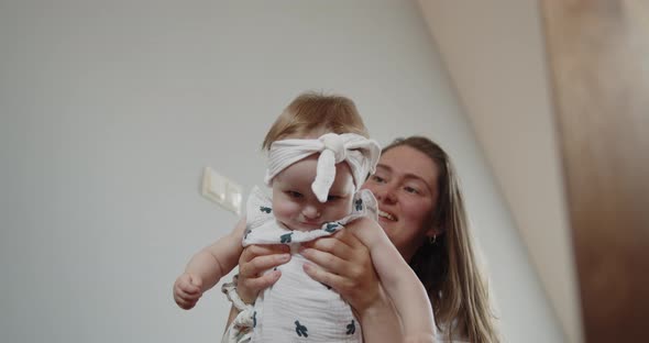 Young Mother Lifts Up Her Cute Baby Daughter Having Fun and Laughing Indoors