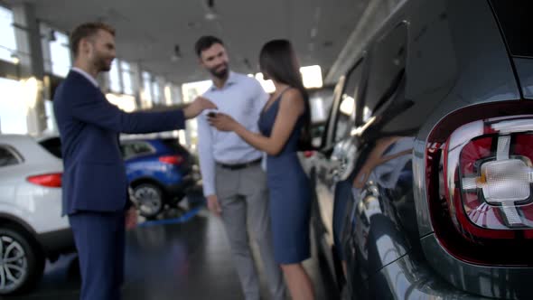 Blurry Joyful Couple Getting Car Key at Dealership