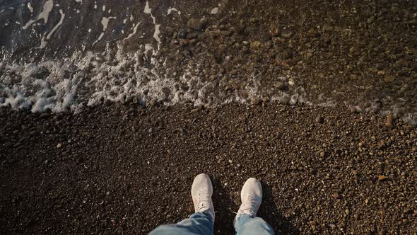 POV First Person View of Mans Legs at Pebble Sea Beach with Waves Rolls on Shore