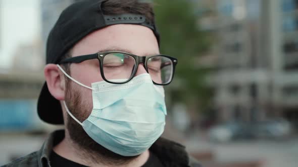 Portrait of Young Man in Glasses Cap and Medical Mask Looks Aside Thoughtfully