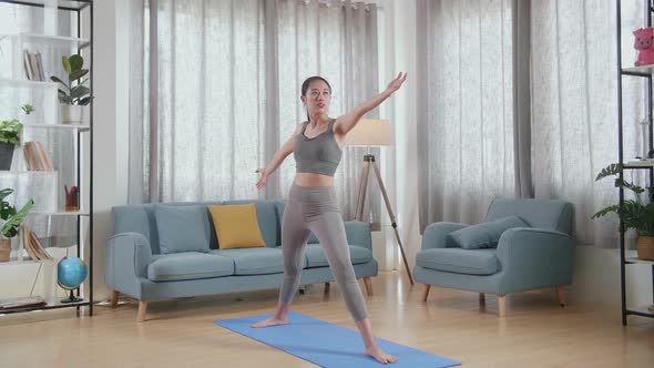 Asian Athletic Female Exercising, Stretching And Practicing Yoga In Warrior Ii Pose At Home