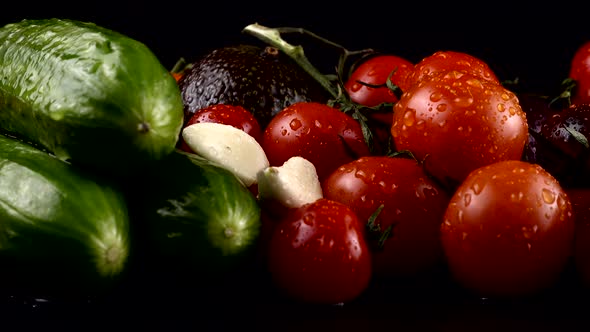 Cherry tomatoes, cucumbers, garlic, avocado and red onion on a black background in water drops