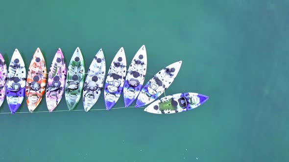 A dynamic top-down aerial shot of colorful kayaks or small watercrafts that are tied up neatly and r