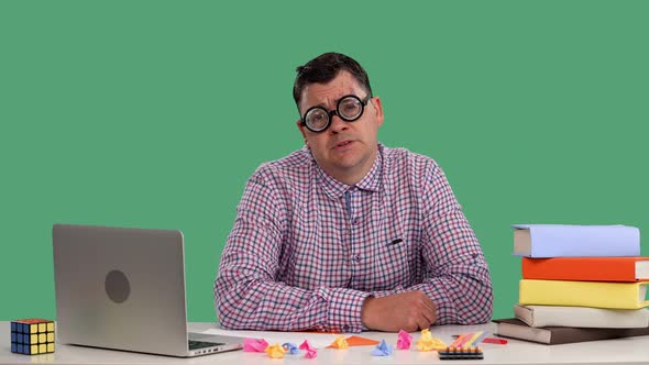 A Tired Man Sits at His Desk in Front of a Laptop Yawning Covering His Mouth with His Palm