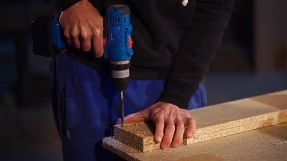 Master Is Drilling Holes in a Wooden Particle Board in a Workshop of Joinery