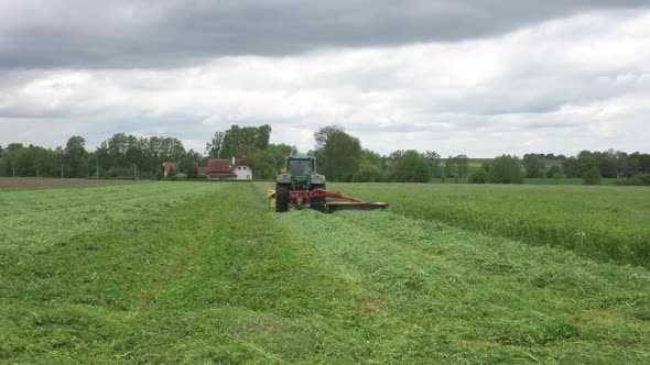 Tractor Mowing Grass in Green Agricultural Field Under Dramatic Sky, Slow Motion Wide View