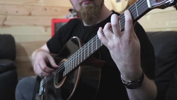 Bearded man playing black acoustic guitar, finger style Medium Shot