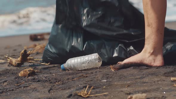 Closeup of Volunteer Picking Up Plastic Bottle on the Black Sand Beach Into Black Plastic Bag