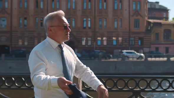 Successful Mature Entrepreneur Putting Off Jacket Walking Outdoors By Riverside