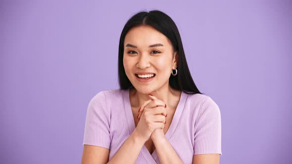 Smiling Asian brunette woman wearing purple t-shirt showing silence gesture