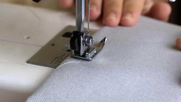 Woman hands with gray fabric sewing with a sewing machine. Women's hands sew on a sewing machine.